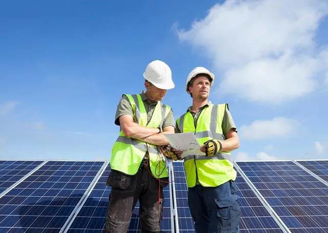 Dwóch pracowników stojących przed panelami słonecznymi